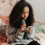 Adolescente souriante qui tape un SMS sur son smartphone dans sa chambre