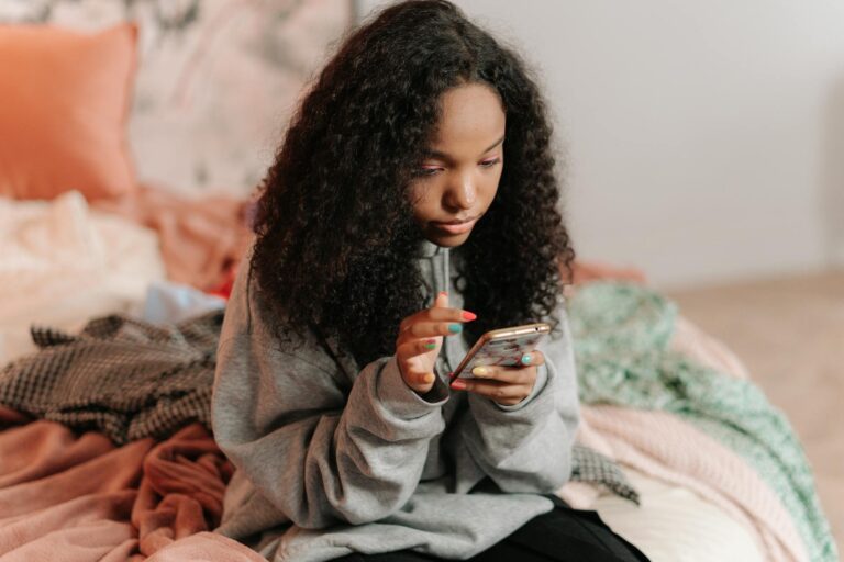 Adolescente souriante qui tape un SMS sur son smartphone dans sa chambre